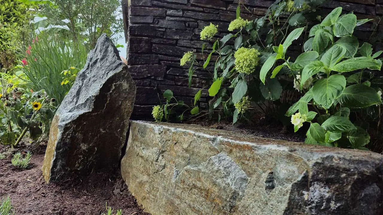 Natursteinmauer mit integrierter Bepflanzung und Solitärstein im Garten.