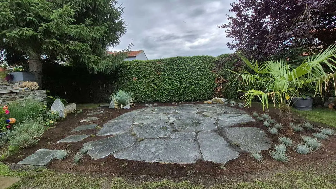 Sitzfläche aus großformatigen Natursteinplatten, eingefasst von Stauden und Gehölzen.