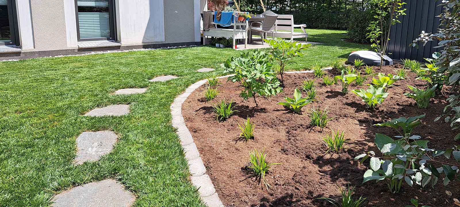 Naturnah gestalteter Garten mit Rasenfläche, geschwungenem Pflanzbeet und Trittsteinen.